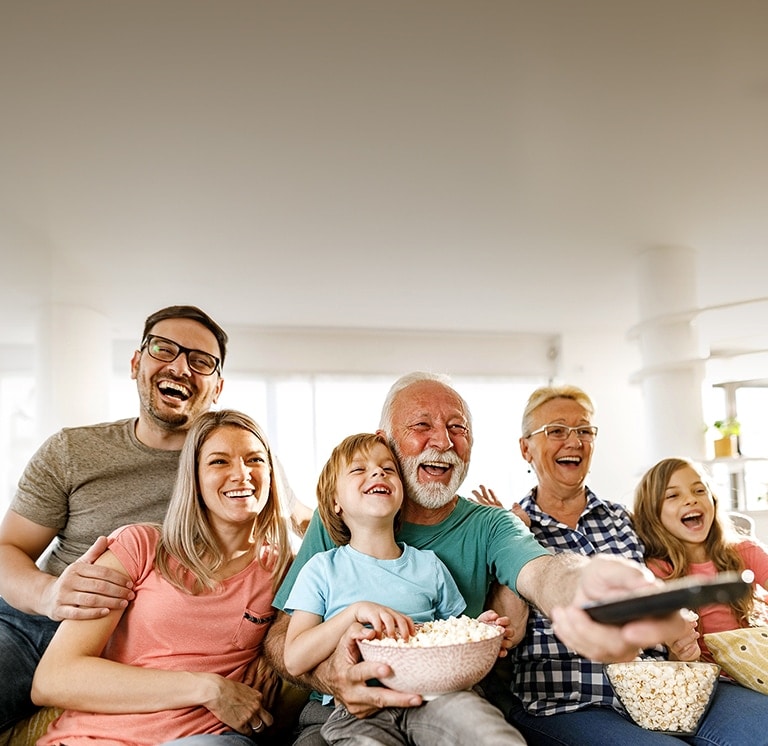 A family sits laughing while the grandfather points the remote outward.