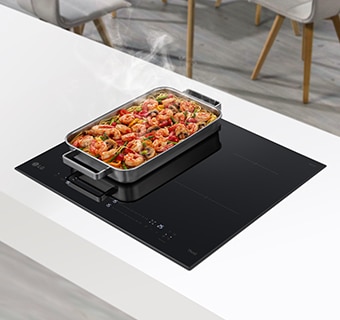 A wide fan is located on two burners In the induction hob. The food on the pan is steaming.