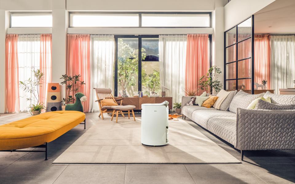 Modern living room with pastel curtains, cozy seating, indoor plants, and an LG Dehumidifier in the center.