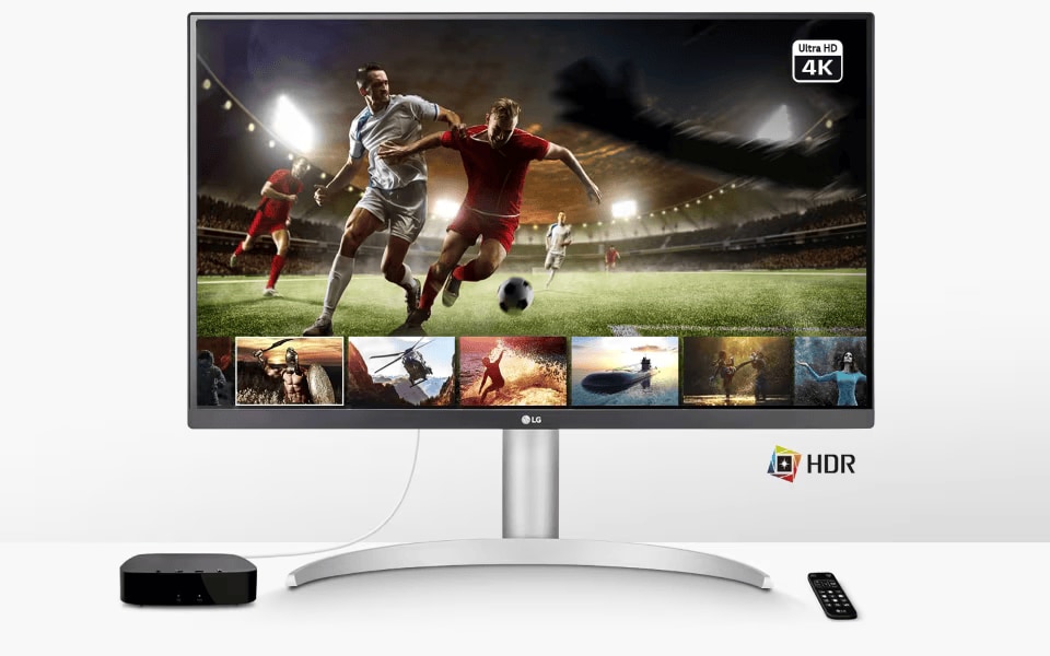 LG monitor showing 4K HDR sports and action scenes, with sleek stand, remote, and media box on white desk.