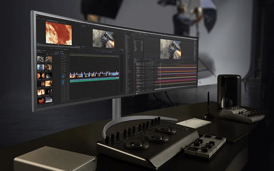 LG Ultrawide Curved monitor with video editing software open, surrounded by editing consoles and tools on a desk.