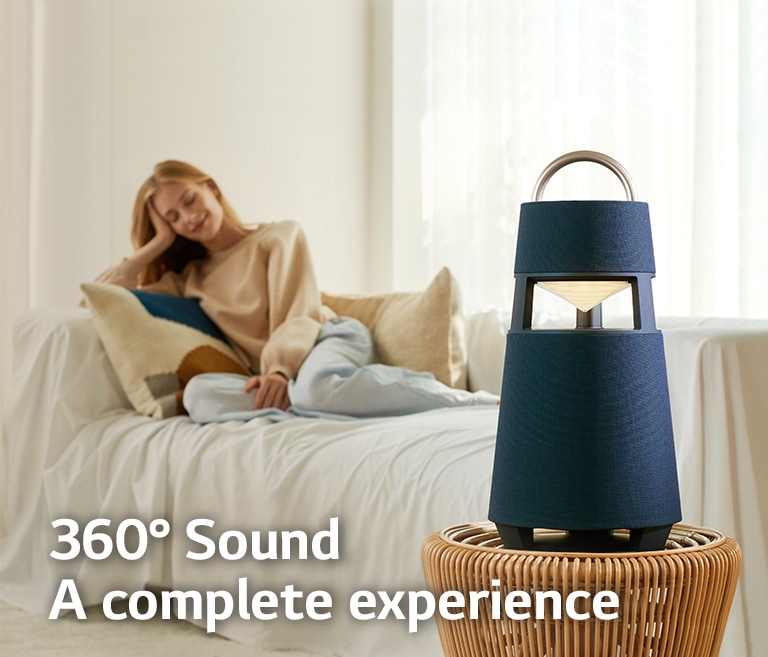 An image of a woman sitting on a sofa listening to music with an XBOOM 360 in front of her.