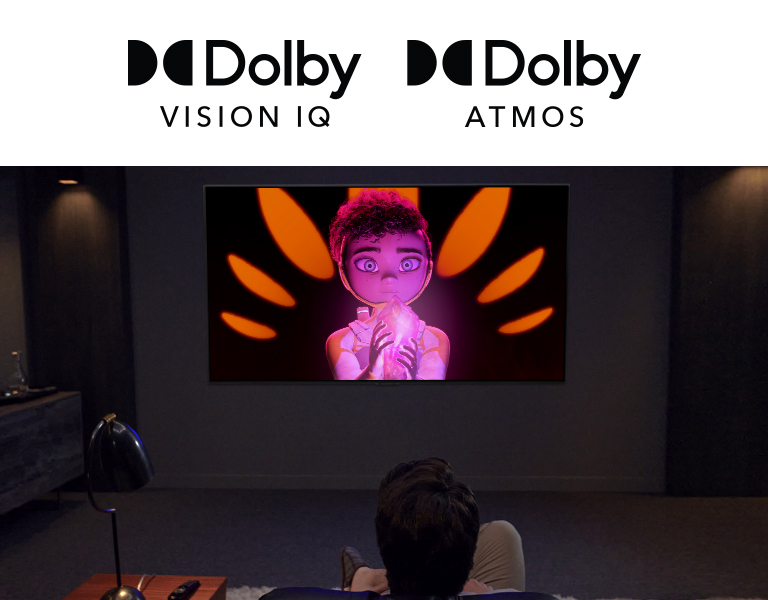 Le logo de Dolby Vision IQ et d’Atmos sont alignés horizontalement. Sous les logos, un père et son fils sont assis sur un canapé et regarde un téléviseur affichant une fille tenant un minérai au milieu d’un arrière-plan noir et orange.