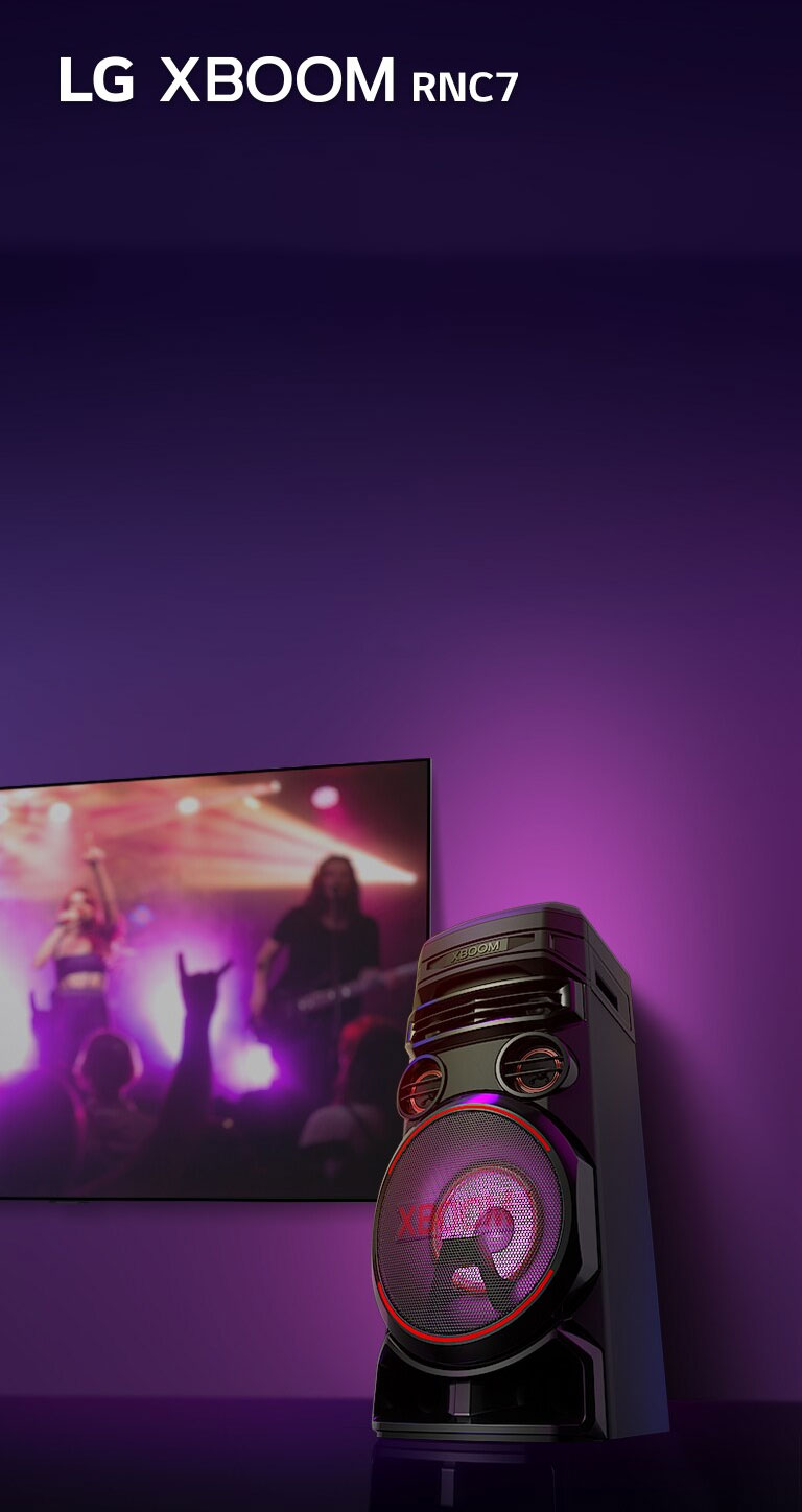 Vue en contreplongée du c?té droit de l’enceinte LG XBOOM RNC5 sur fond violet.  L’éclairage du XBOOM est également violet. Et un écran de télévision diffuse un concert.