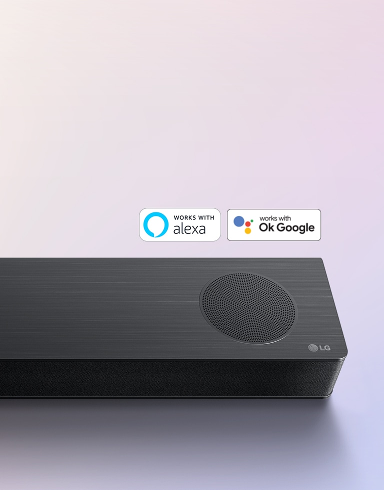 La barra de sonido LG se encuentra en el suelo y muestra el logotipo de LG en la esquina derecha de la barra de sonido. El logotipo de Alexa y los logotipos de OK GOOGLE se encuentran en la barra de sonido.