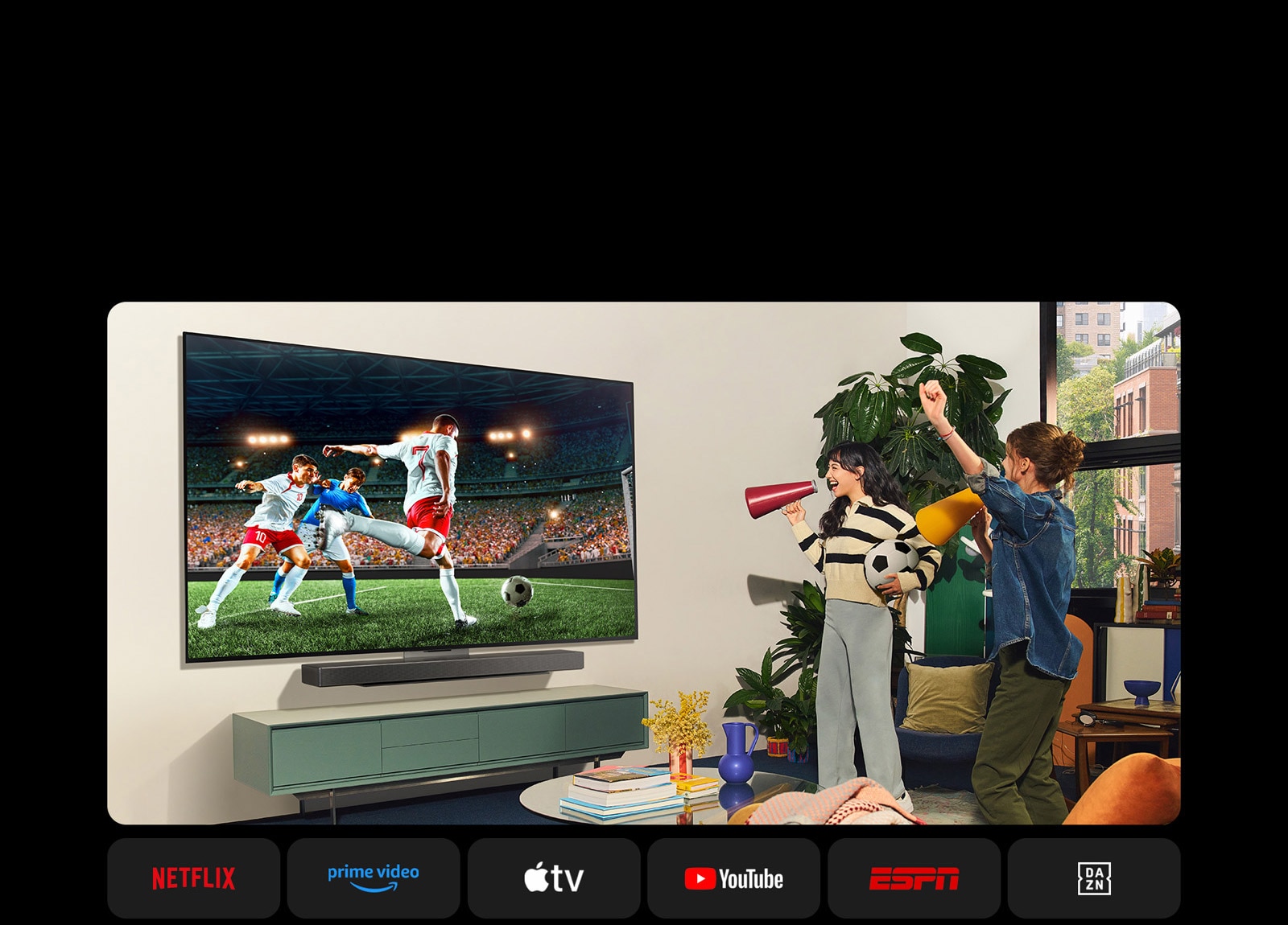 Dos mujeres ven un partido de fútbol en una acogedora sala. Una mujer sostiene una pelota de fútbol y ambas animan a su equipo con altavoces amarillos y rojos. Los siguientes logos se muestran a continuación. Netflix, Amazon Prime Video, Apple TV, Youtube, ESPN y DAZN.