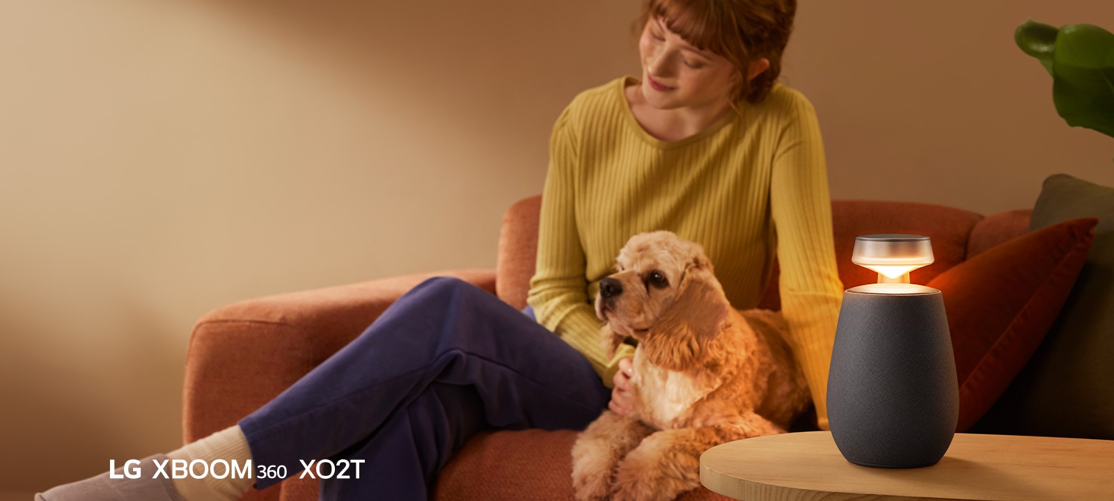 A woman sitting on the sofa with her dog and listening music with LG XBOOM 360 XO2T.