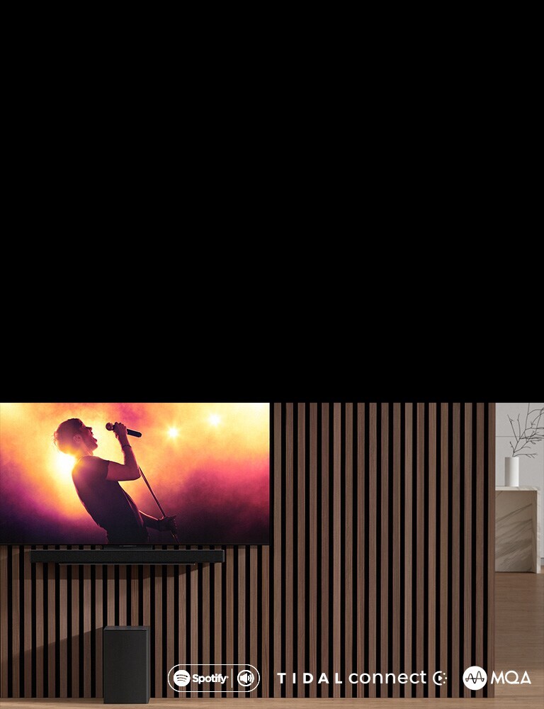LG OLED C 掛在墻壁上，下方使用專用支架放置 LG 無線環繞回音壁 SC9S。音箱底下放置著超低音音箱。電視正播放音樂會的場景。
