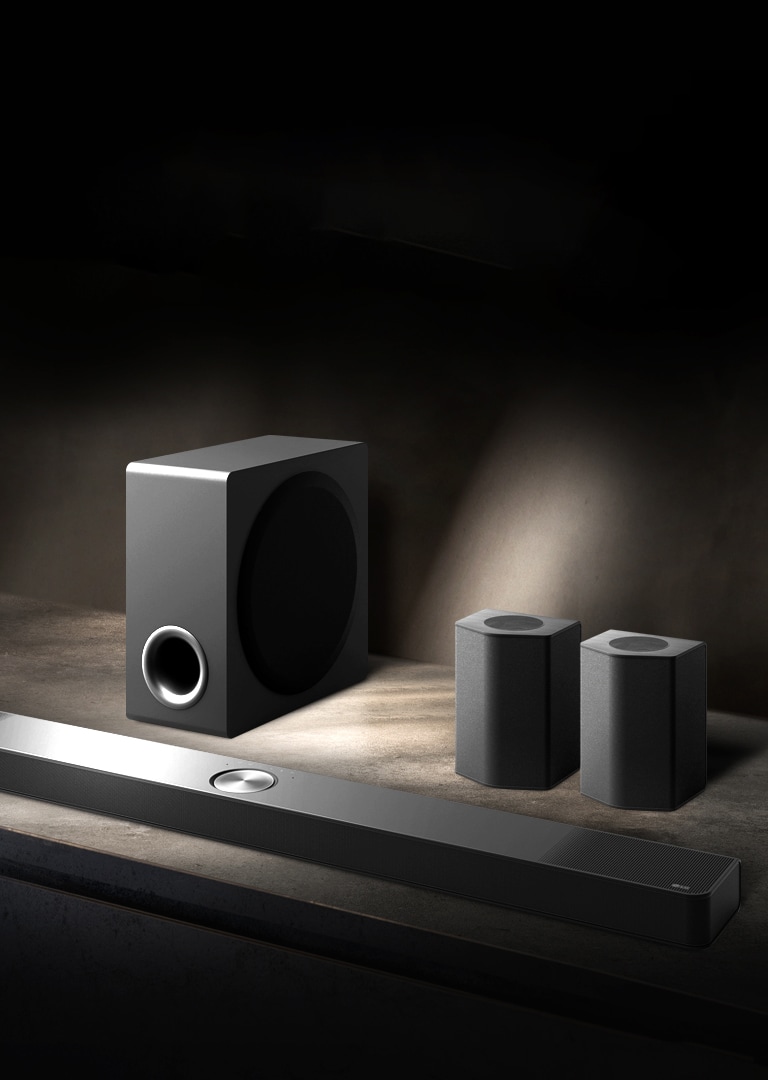 LG Soundbar、后置揚聲器和低音炮（傾斜視圖）位于黑色房間的褐色木架，籠罩在黑暗中，光線只照在音箱系統。