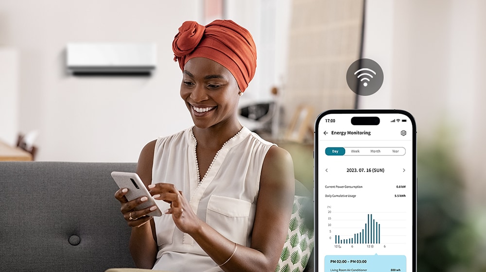 Eine Frau genie?t den kühlen Luftstrom der Klimaanlage und überprüft deren Energieverbrauch über den Bildschirm der ThinQ?-App.