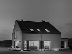 Au?enger?t zwischen einer verschneiten Ziegelwand und einem zweist?ckigen Haus mit gro?em Fenster, durch die man ins Wohnzimmer blicken kann.