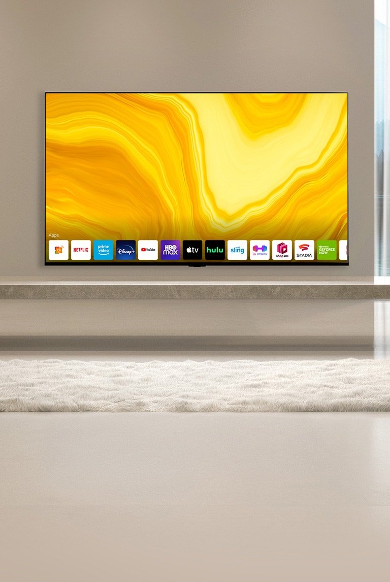 Auf dem Startbildschirm wird nach unten gescrollt und die Szene wechselt zu einem Fernseher, der in einem in warmen Farben eingerichteten Wohnzimmer h?ngt und den Startbildschirm anzeigt. 