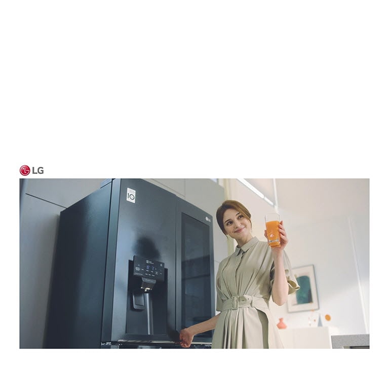 Eine Frau steht vor dem Kühlschrank, h?lt ein Glas Saft in der Hand und l?chelt, als sie die Tür schlie?t.