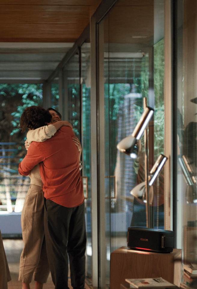 Eine Frau und ein Mann umarmen sich im Wohnzimmer, w?hrend der XBOOM-Lautsprecher neben ihnen eingeschaltet ist.