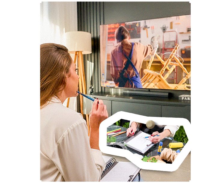 Carol assistindo a um vídeo de DIY na TV enquanto desenha ideias em um caderno, com destaque para m?os montando um mood board.