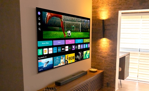 TV LG OLED pendurada na parede, operando com webOS na tela. Vários ícones de plataforma e servi?o na tela do webOS.