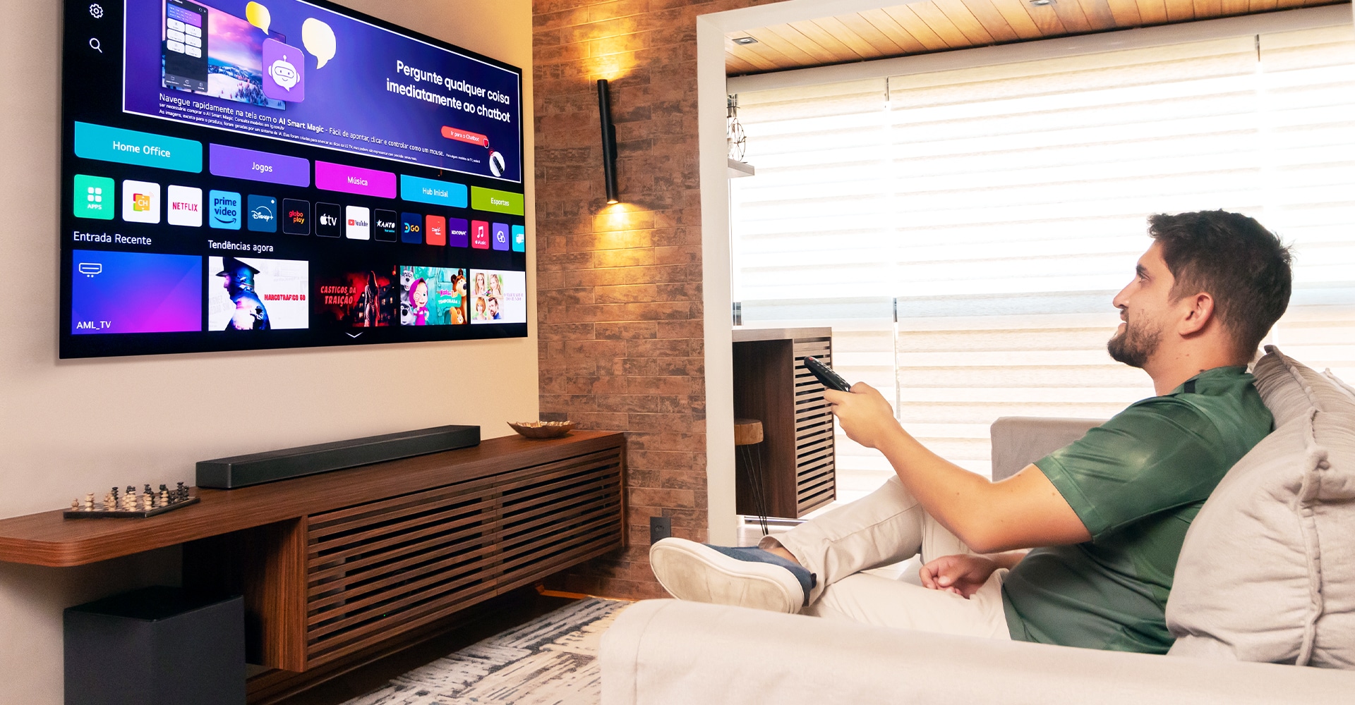 O editor especial Enzo está sentado em um sofá, segurando um controle remoto para operar a TV LG OLED. A fun??o WebOS está sendo exibida na tela.