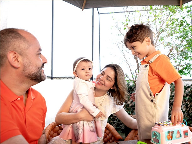 Cortado de família, sorrindo felizmente. A m?e segurava a filha nos bra?os, o pai e o filho também pareciam bonitos. O filho a segurar o brinquedo.