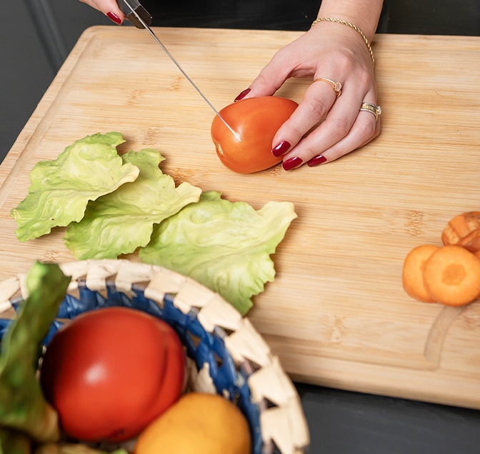 A m?e cortou um tomate vermelho. Algumas cenouras já foram cortadas, tomate e outros vegetais na tigela.