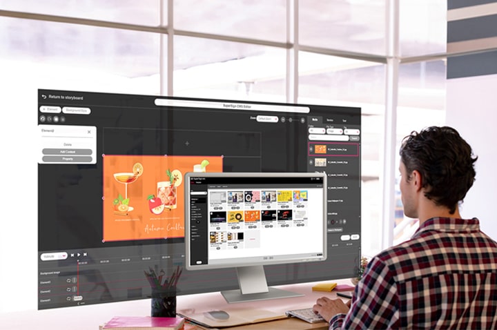 Homem criando conteúdo para a sinaliza??o. A tela do monitor exibe uma lista do conteúdo gerado, enquanto um editor para cria??o de conteúdo em uma tela maior também é apresentado. Ambas as telas fornecem visualiza??es genuínas acessíveis dentro da solu??o.