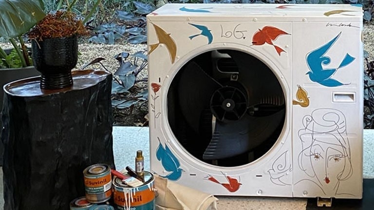 área externa do condensador LG Smart Inverter personalizada por um artista com desenhos coloridos enquanto potes de tinta empilhados à direita.