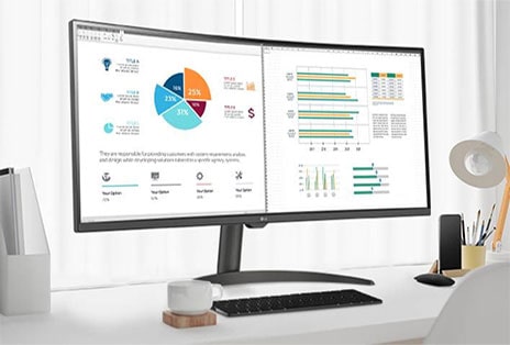 Na mesa, há um monitor inteligente, exibindo um documento de home office sendo trabalhado. à esquerda do monitor, há um copo com al?a e, à direita, um telefone celular, um porta-lápis e um suporte.