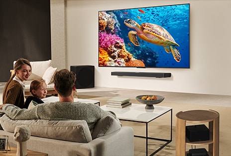 Une famille est assise sur un canapé face à un LG TV monté sur un mur au-dessus d’une LG Soundbar. La bo?te Zero Connect se trouve à l’intérieur d’une table basse.
