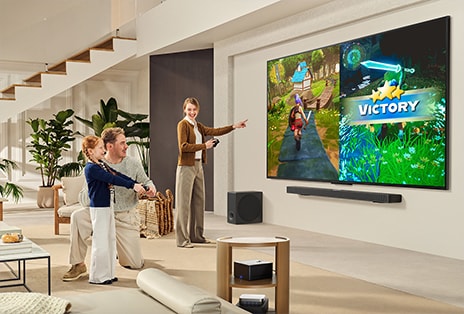 La bo?te Famille de 3?personnes jouant à un jeu dans un salon avec un LG TV monté sur un mur au-dessus d’une LG Soundbar. La bo?te Zero Connect se trouve à l’intérieur d’une table basse.