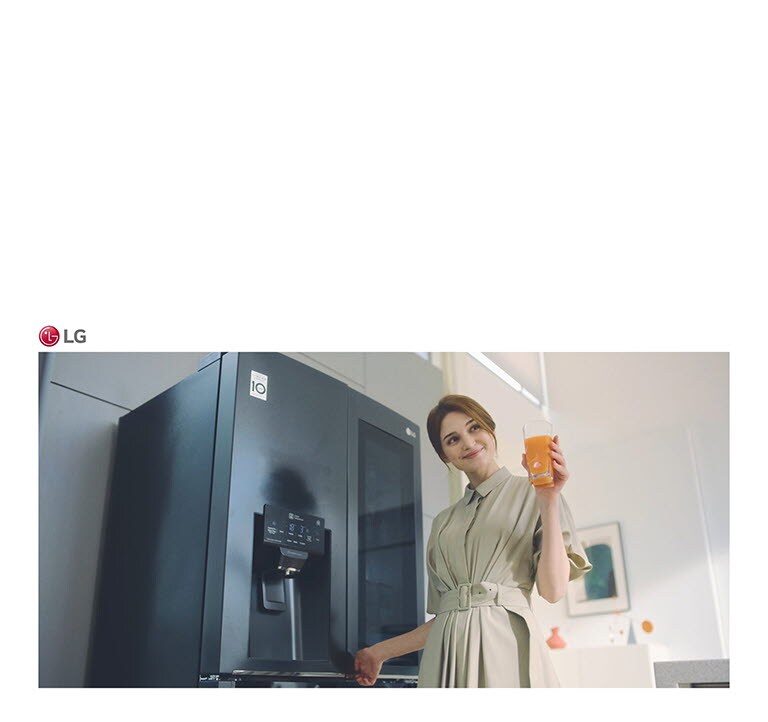 Eine Frau steht vor dem Kühlschrank, h?lt ein Glas Saft in der Hand und l?chelt, als sie die Tür schlie?t.