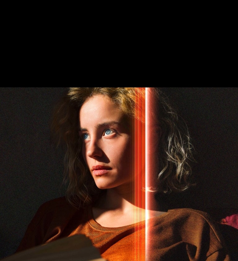 Eine Frau mit strahlend blauen Augen und einem orangefarbenen Oberteil in einem dunklen Raum. Rote Linien, die AI-Verfeinerungen darstellen, bedecken einen Teil ihres Gesichts, das hell und detailliert ist, w?hrend der Rest des Bildes stumpf aussieht. 