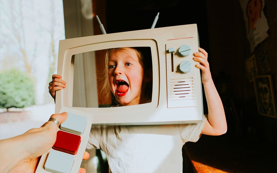 Ein Kind h?lt einen ausgeschnittenen Fernseher hoch, w?hrend ein Erwachsener eine Spielzeugfernbedienung h?lt, die den Prozess der Kalibrierung eines Fernsehers darstellt