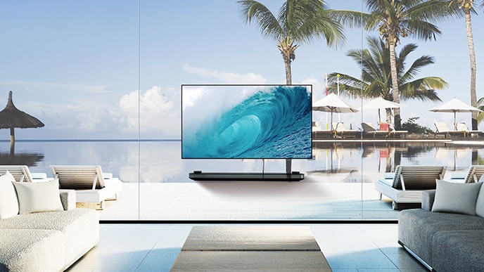 LG SIGNATURE OLED TV W montre la vague fra?che sur son écran tout en étant posé dans le salon avec la vue sur l'océan bleu au-delà de la fenêtre.