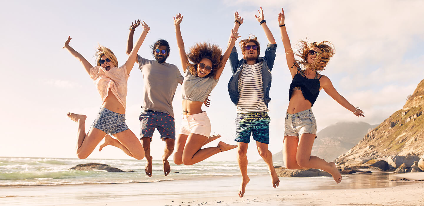 Grupo de amigos saltando en la playa con el parlante LG XBOOM XL7S en primer plano.