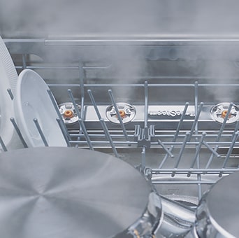 Primer plano de platos y vasos siendo lavados al vapor dentro del lavavajillas.