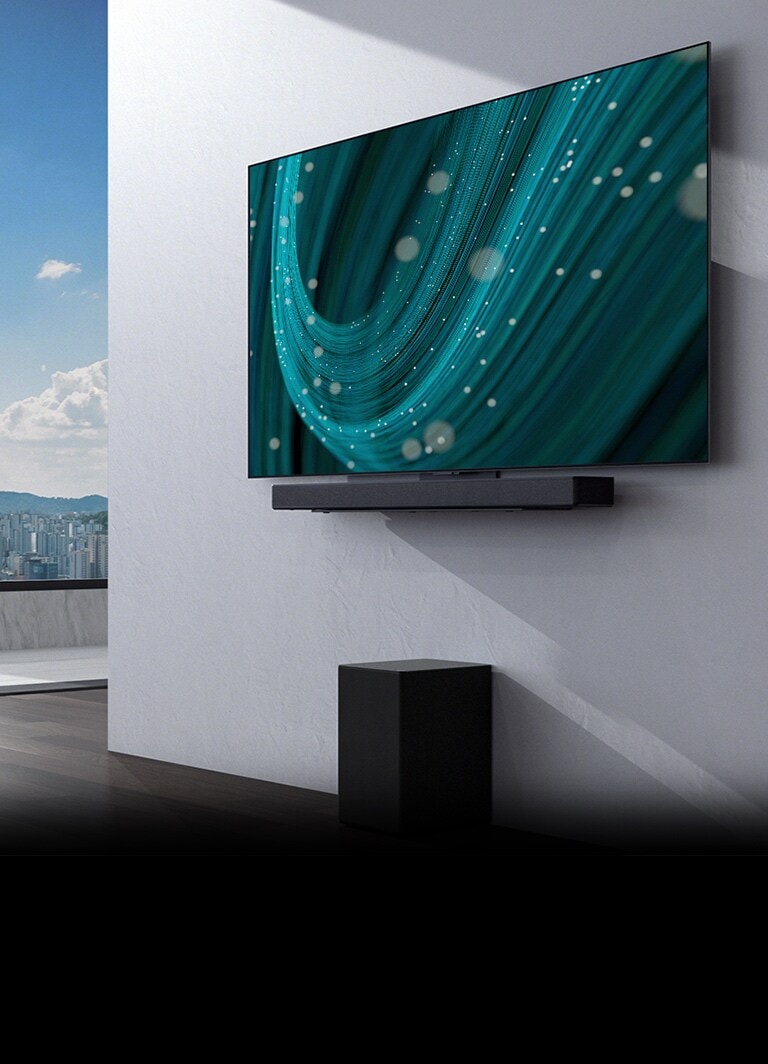 En el centro de un espacio con una ventana grande, hay una pared con un televisor y una barra de sonido montados encima y ??un subwoofer debajo. La pantalla muestra una imagen de fondo de color verde azulado.