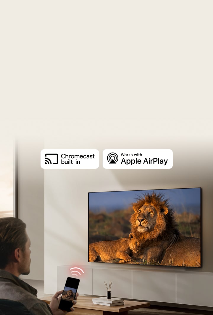 En LG TV monterad p? en v?gg i ett vardagsrum och visar ett lejon och en lejonunge. En man sitter i f?rgrunden med en smartphone i handen som visar samma bild av lejon. En grafik av tre neonr?da b?jda staplar visas precis ovanf?r smarttelefonen och pekar mot TV:n.