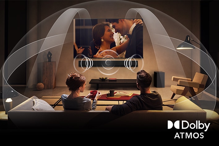 Tlumeně osvětleny obyvák s OLED LG TV a LG Soundbarem. Na obrazovce je záběr na hrající elektrickou kytaru. Grafika ukazuje, jak Dolby Atmos naplní prostor zvukem. Logo Dolby Atmos je ve spodním rohu.