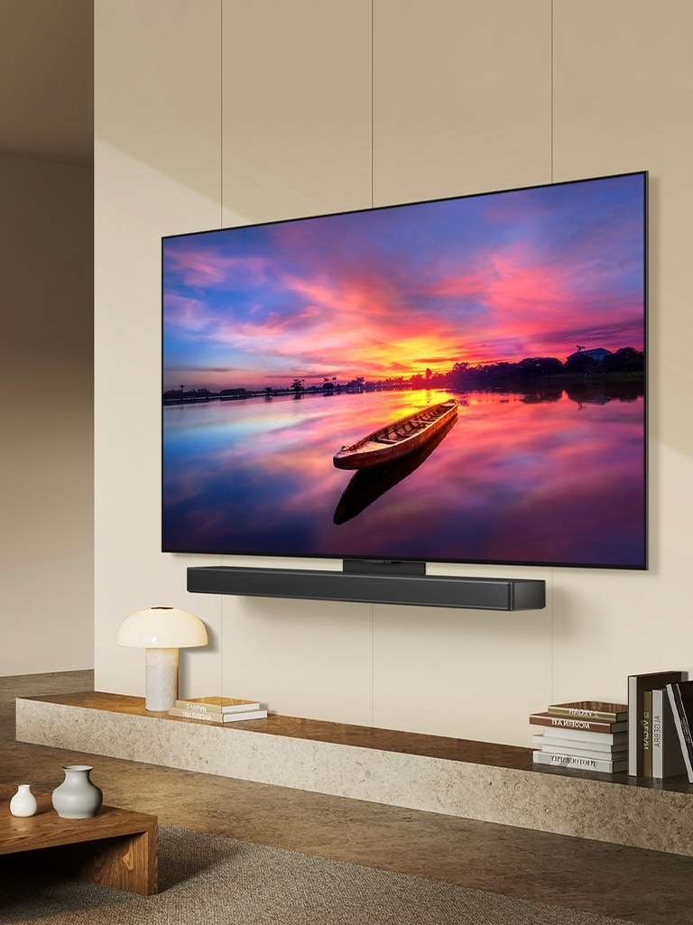 LG OLED TV, OLED C4 oto?eny o 45 stupň? doleva a zobrazující krásny západ slunce s lodí na jeze?e, jak je televizor p?ipojen k soundbaru LG Soundbar pomocí dr?áku Synergy v minimalistickém obyvacím prostoru.