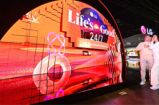 Náv?těvníci sledují zak?iveny LED displej LG s heslem ?Life’s Good 24/7“ na technologické vystavě