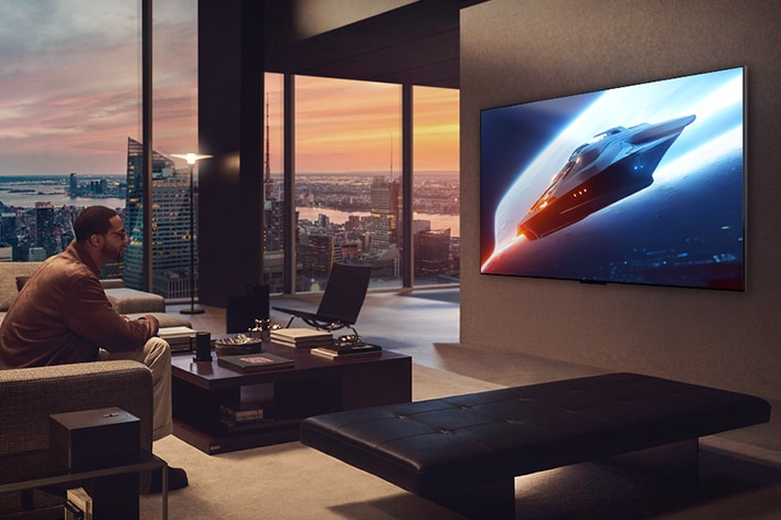 Stilvolles Wohnzimmer in einer Penthouse-Wohnung. Wundersch?ne Stadtansicht durch das Fenster. Ein Mann sitzt auf der Couch und sieht auf den an der Wand befestigten Fernseher. 