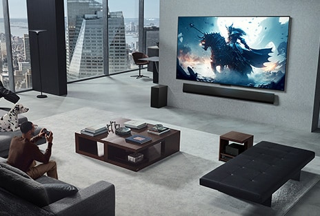 Wohnzimmer mit einer Person, die ein Video-Game auf einem an der Wand montierten LG True Wireless TV mit LG Soundbar spielt. Sie h?lt einen Controller in der Hand, aber die Spielkonsole ist nicht sofort zu sehen. Es sind auch keine Kabel zu sehen. Die Zero Connect Box steht versteckt unter einem Beistelltisch.