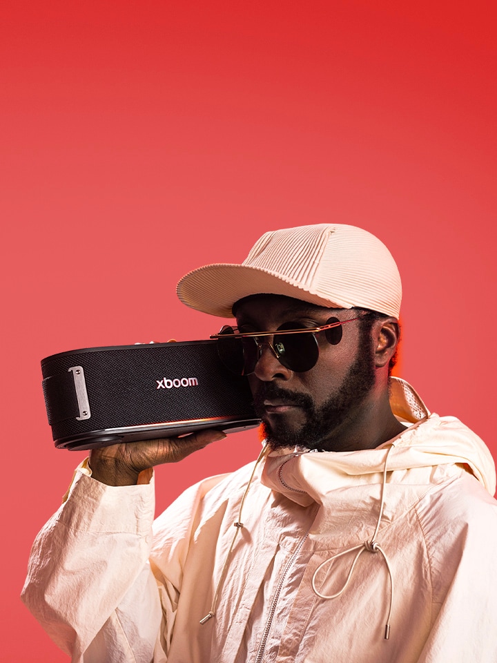 will.i.am in wei?em Outfit und Sonnenbrille h?lt xboom Bounce direkt neben sein Gesicht.	