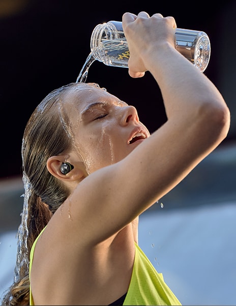 Eine Frau gie?t sich Wasser ins Gesicht und hat DTDTF7QF8 am Ohr.