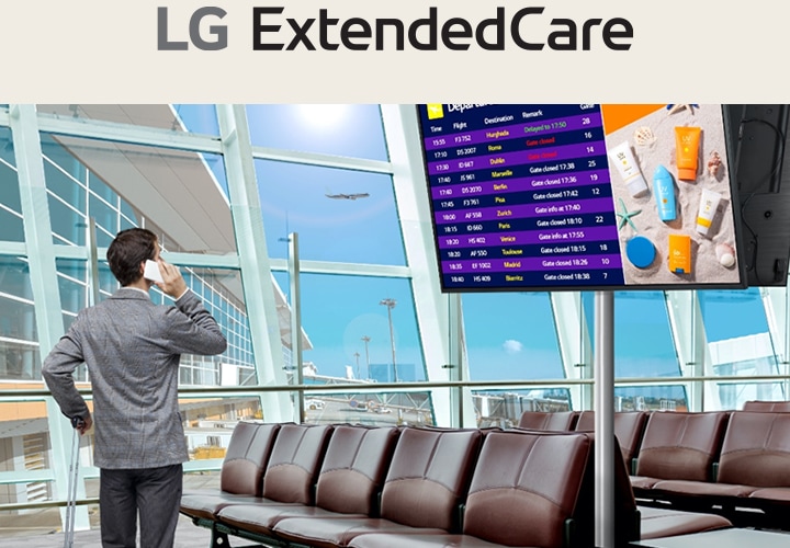 Ein Reisender steht in einer Flughafenlounge und überprüft sein Telefon, w?hrend er auf ein digitales Abflugbrett schaut, das Flugpl?ne anzeigt. Die Szene unterstreicht die moderne, effiziente Nutzung von Beschilderungen für Echtzeit-Updates.