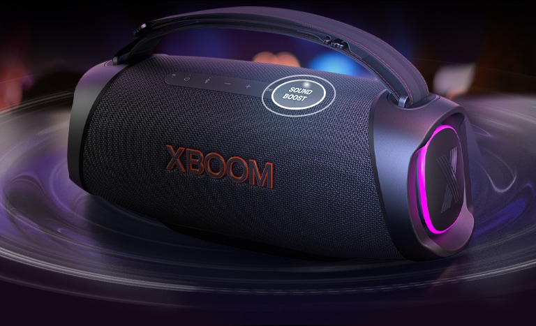 Der LG XBOOM Go DXG8T ist auf dem Tisch platziert. Die Sound-Boost-Taste ist vergr??ert und unter dem Lautsprecher sind Schallwelleneffekte zu sehen. 