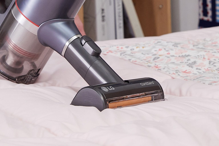 Die Power Punch-Düse für Polsterm?bel wird mit dem Beh?lter gezeigt, der Schmutz und Staub von einem Bett entfernt.
