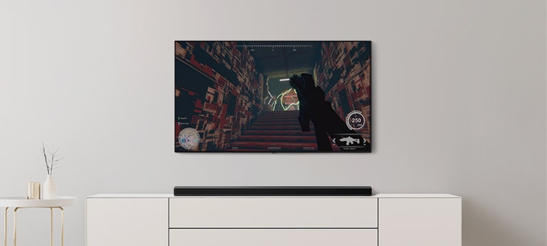 In einem Wohnzimmer befinden sich ein TV und eine Soundbar. Auf dem TV-Bildschirm l?uft ein FPS-Spiel und der TV-Kanal ist auf Fu?ballspiel eingestellt (Video abspielen).