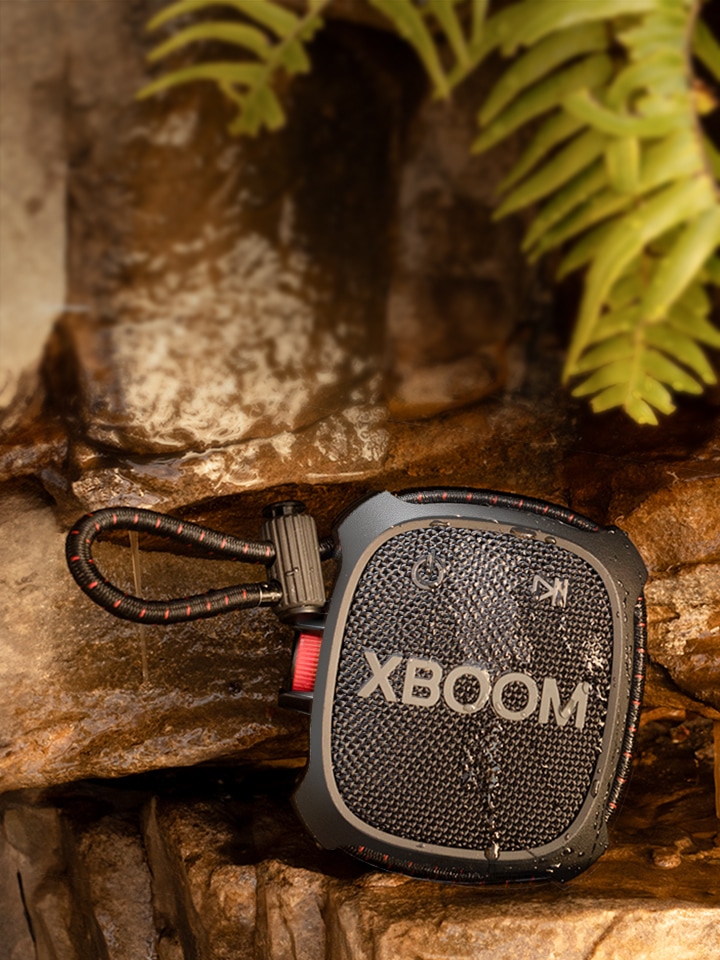 Ein Mann sitzt auf dem Boden und h?rt Musik mit einem LG XBOOM Go XG2T, das an seinem Rucksack h?ngt.