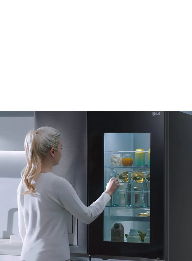 Ein Video zeigt eine Frau, die sich ihrem InstaView-Kühlschrank n?hert und zweimal anklopft. Der Innenraum leuchtet auf, und sie kann den Inhalt ihres Kühlschranks sehen, ohne die Tür ?ffnen zu müssen. Die Ansicht zoomt heran, sodass die Getr?nke in der Tür zu sehen sind, und zoomt dann heraus, um die Frau von hinten zu zeigen, wie sie die Tür ?ffnet und sich ein Getr?nk nimmt.