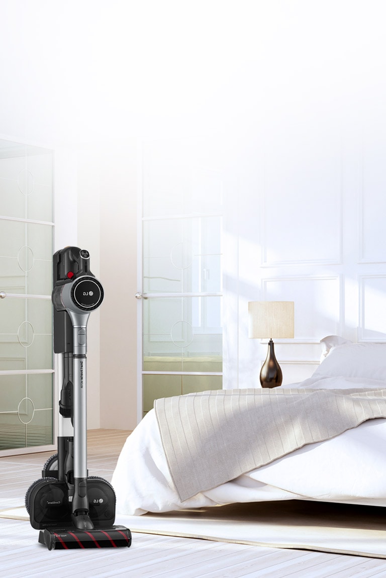 Der CordZero A9 Kompressor-Staubsauger steht in der Ladestation in einem Schlafzimmer neben einem Bett.